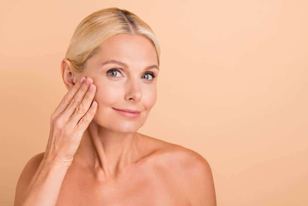 A woman who has had a facelift and is touching her face.