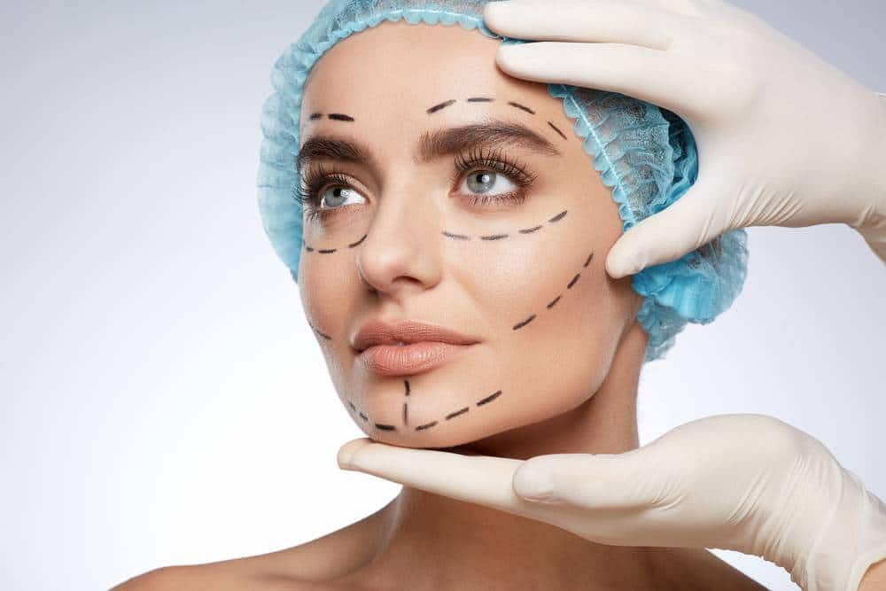 A young woman being prepped for a facelift, with lines drawn on her face and wearing a blue cap.
