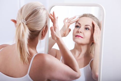A middle aged woman looking at herself in the mirror.