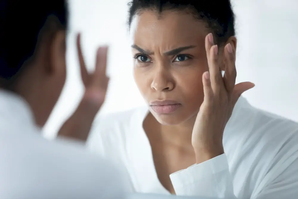 A woman looking at her face in the mirror and frowning