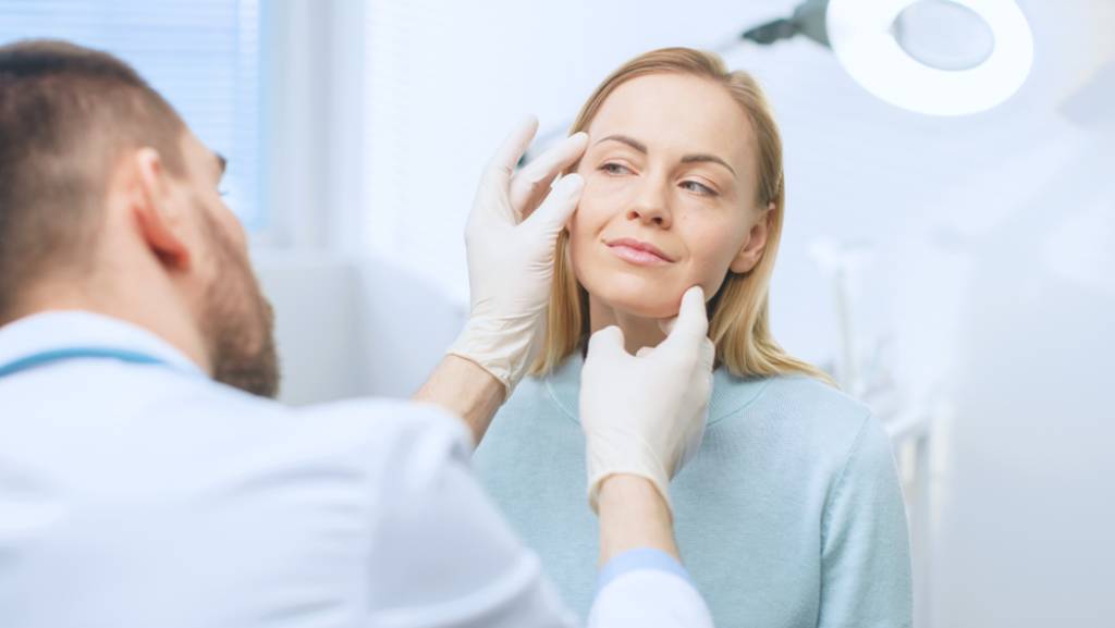 A plastic surgeon examining around a patient’s eyes.