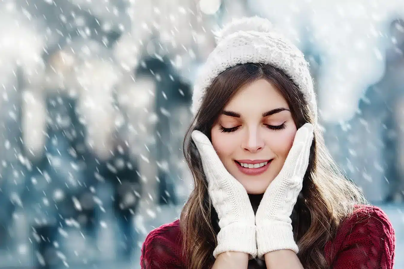 Beautiful young woman in the snow with glowing skin, mittens, and a hat.